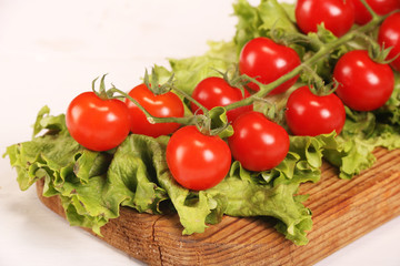 Ripe fresh Juicy organic brunch of cherry tomatoes on cutting board with Green Lettuce on a white table
