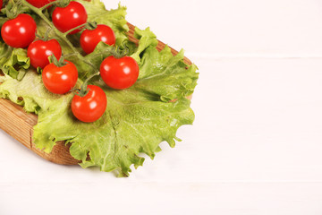 Ripe fresh Juicy organic brunch of cherry tomatoes on cutting board with Green Lettuce on a white table