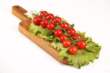 Ripe fresh Juicy organic brunch of cherry tomatoes on cutting board with Green Lettuce on a white table