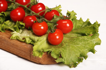 Ripe fresh Juicy organic brunch of cherry tomatoes on cutting board with Green Lettuce on a white table