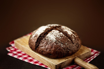 Freshly baked bread on wooden cutting board over  dark rustic wooden background closeup
