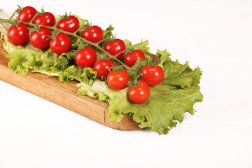 Ripe fresh Juicy organic brunch of cherry tomatoes on cutting board with Green Lettuce on a white table