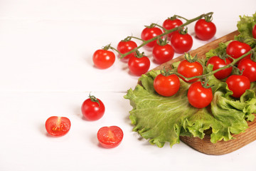 Ripe fresh Juicy organic brunch of cherry tomatoes on cutting board with Green Lettuce on a white table
