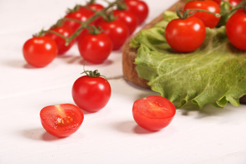 Ripe fresh Juicy organic brunch of cherry tomatoes on cutting board with Green Lettuce on a white table