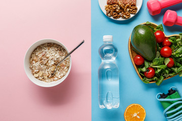 top view of bottle with water, diet food, sport equipment on blue and pink background