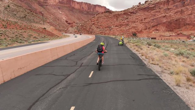 Tourists (family) are biking in Moab, Utah. Scenic bikeway, huge red sandstone cliffs. Moab canyon pathway, paved bike trail.