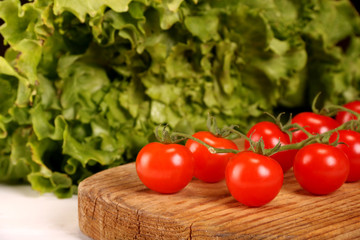 Ripe fresh Juicy organic brunch of cherry tomatoes on cutting board with Green Lettuce on a white table