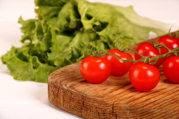 Ripe fresh Juicy organic brunch of cherry tomatoes on cutting board with Green Lettuce on a white table