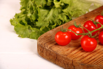 Ripe fresh Juicy organic brunch of cherry tomatoes on cutting board with Green Lettuce on a white table