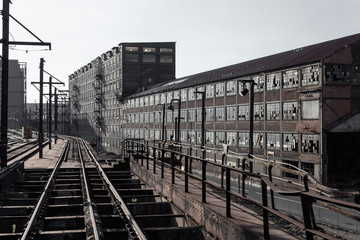 Fototapeta na wymiar View down railroad tracks alongside abandoned industrial buildings, horizontal aspect