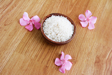 Fototapeta na wymiar white natural rice in a brown wooden plate and decorative pink flowers on yellow background