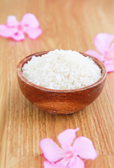 Obraz na płótnie Canvas white natural rice in a brown wooden plate and decorative pink flowers on yellow background