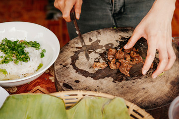 Close up hands chopping Asian barbeque stewed pork on old wood cutting board for rice noodle soup - Asian style street food