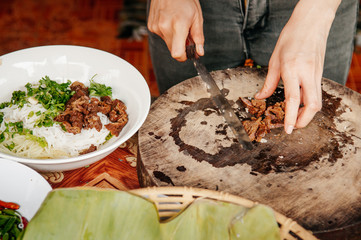 Close up hands chopping Asian barbeque stewed pork on old wood cutting board for rice noodle soup - Asian style street food