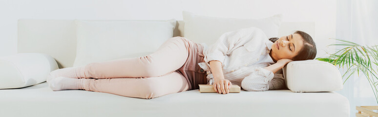 panoramic shot of beautiful latin woman sleeping with book on couch at home
