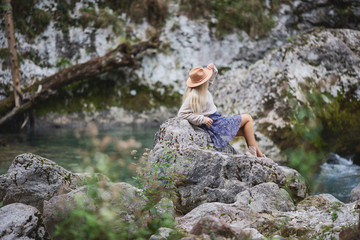 A girl sitting on the stone among the mountains and looking at the river. Woman sits near the mountain river enjoy the view. The rapids on the river