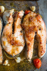 Grilled salmon steak with addition of lemon, rosemary, garlic, onion and spices on grill plate, top view. Grilled fish, seafood