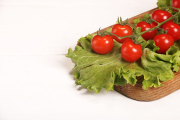 Ripe fresh Juicy organic brunch of cherry tomatoes on cutting board with Green Lettuce on a white table. Copy space