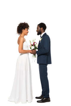 happy african american bride holding bouquet near bridegroom isolated on white