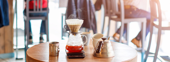 Closeup of coffee brewing gadgets on wooden table in cafe. Drip brewing, filtered coffee, or pour-over is a method which involves pouring water over roasted, ground coffee beans contained in a filter