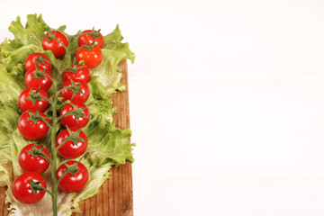Ripe fresh Juicy organic brunch of cherry tomatoes on cutting board with Green Lettuce on white table. Top view