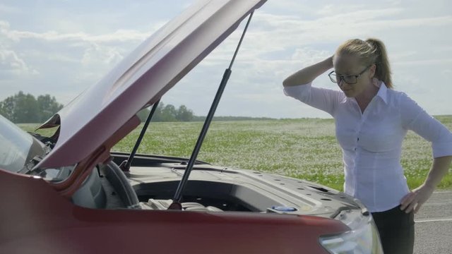 woman expresses bewilderment when she looks under hood of car.