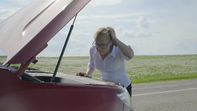 woman expresses bewilderment when she looks under hood of car.