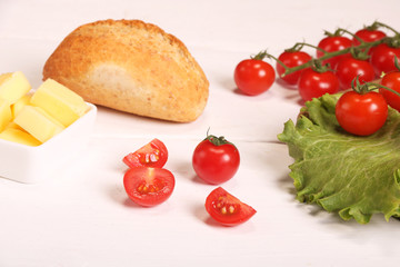 Ripe fresh Juicy organic brunch of cherry tomatoes on cutting board with Green Lettuce, bread, butter on a white table