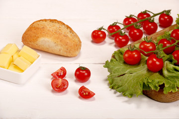 Ripe fresh Juicy organic brunch of cherry tomatoes on cutting board with Green Lettuce, bread, butter on a white table