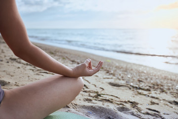 Fototapeta na wymiar Woman sitting on the beach in lotus pose and meditating, body part, doing yoga exercise outdoors, zen balance and relaxation concept