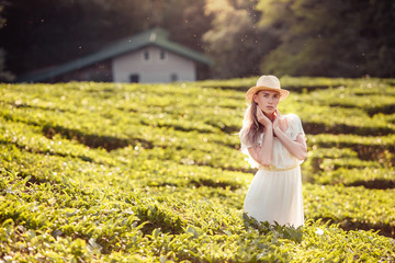 Beautiful romantic young girl in light peasant dress and a hat enjoying a walk around the tea...