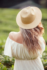 Rear view of a young girl In a bright peasant dress and hat enjoying green bushes and nature and...