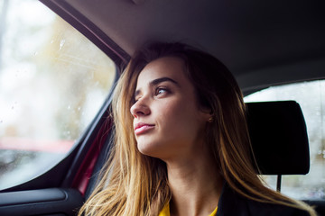Fototapeta na wymiar Beautiful young businesswoman sitting on back seat of a car and looking outside the window