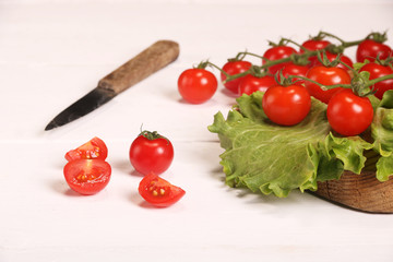 Ripe fresh Juicy organic brunch of cherry tomatoes on cutting board with Green Lettuce and knife on a white table
