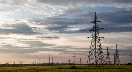 Powerful lines of electric gears.Power lines and sky with clouds.Wires over the fields.Electric power industry and nature concept.High voltage power lines.Field and aerial lines, silhouettes at dusk.