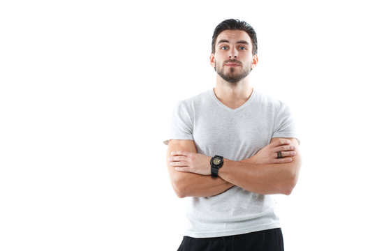 A charismatic young athletic man in a light tight shirt stands with arms crossed over his chest isolated on a white background.