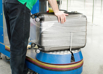 Worker wraps suitcase with a transparent film before travel by airplane for security reason and...
