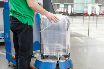 Worker wraps suitcase with a transparent film before travel by airplane for security reason and...