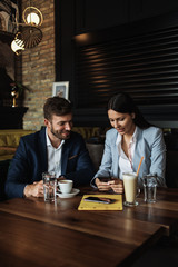 Happy couple man and woman sitting in modern cafe bar or restaurant and drinking coffee.