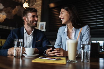 Happy couple man and woman sitting in modern cafe bar or restaurant and drinking coffee.