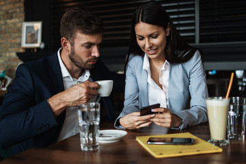 Happy couple man and woman sitting in modern cafe bar or restaurant and drinking coffee.