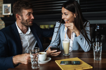 Happy couple man and woman sitting in modern cafe bar or restaurant and drinking coffee.