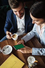 Mockup image of a business people holding smart mobile phone with blank green screen on vintage wooden table in modern cafe restaurant during meeting or lunch.