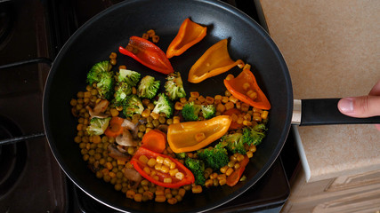 Delicious fresh vegetables are stewed in a pan, food for vegetarians at home. Concept of: Veg, Bio Product, Mushrooms, Broccoli, Colored Cabbage, Carrot, Corn, Paprika.