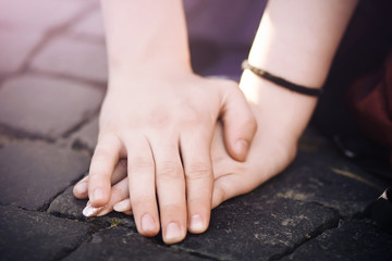 A man's hand with care and love covers a woman's hand, which leaned on the stone pavement, illuminated by the evening sun