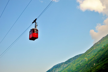 ropeway and funicular road in mountain, red cabin against a background of blue cloudy sky