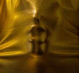 human face pressing through golden fabric