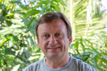 Portrait of a middle aged man resting on a background of green leaves, close up