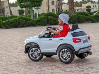 a girl of 3.5 years in a hat and glasses rides on a white toy electric car