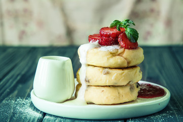 Close up. Traditional rustic breakfast. Delicious cheese pancakes, poured with cream and decorated with strawberries. Copy space.